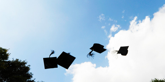 Four black doctor hats flying in the air in front of blue sky with white clouds.